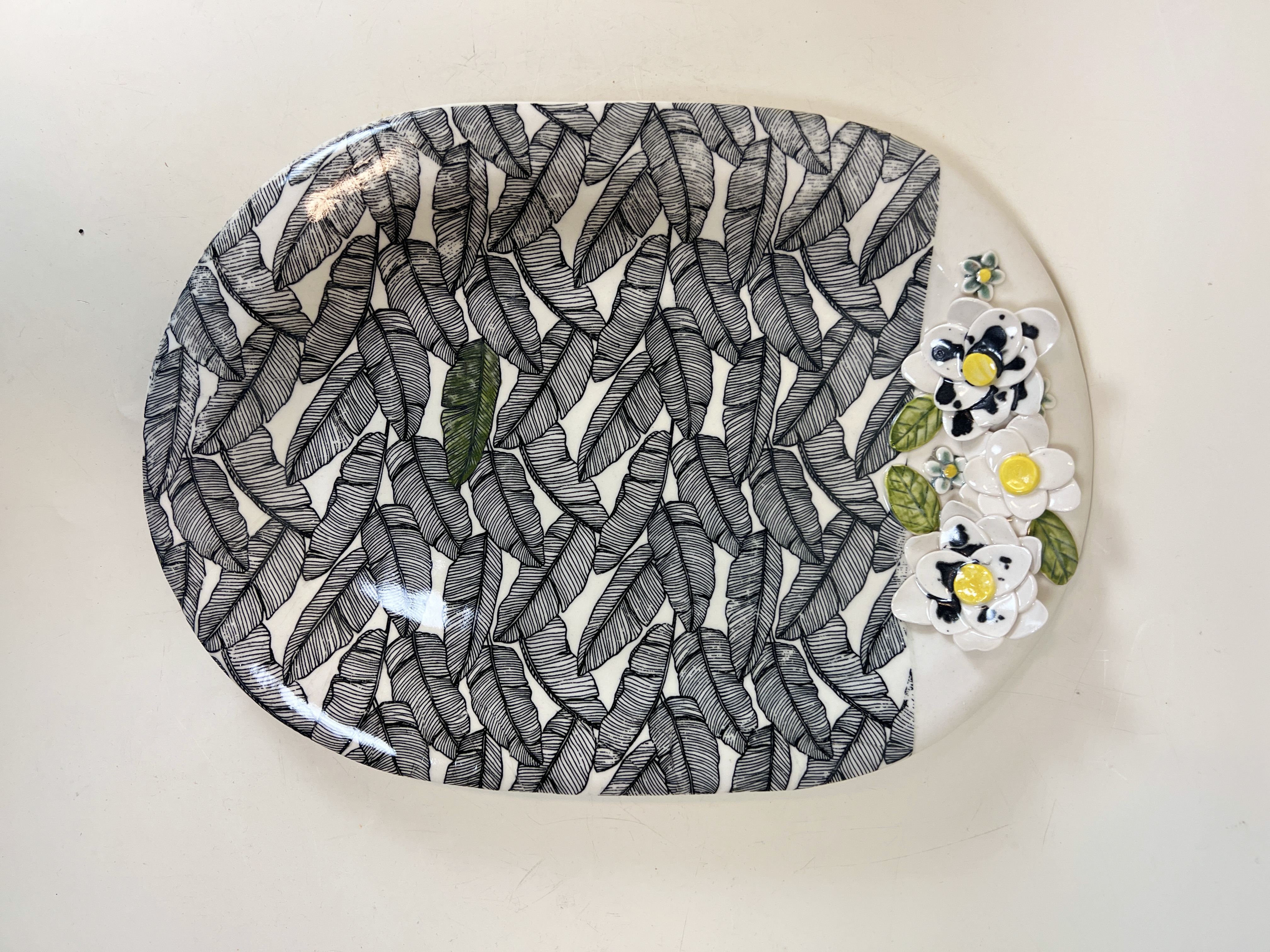 Large oval ceramic platter with dense black and white banana leaf pattern and dimensional white flowers